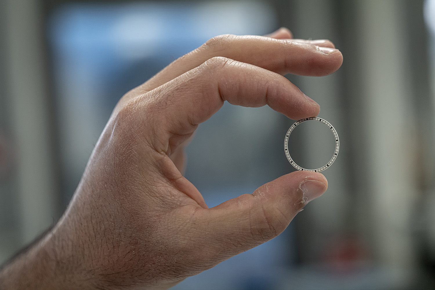 Hand holding up a white stamped thin metal ring between fingers